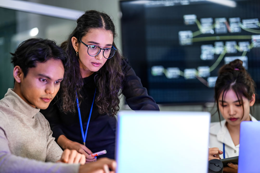 Three office workers looking at a laptop.