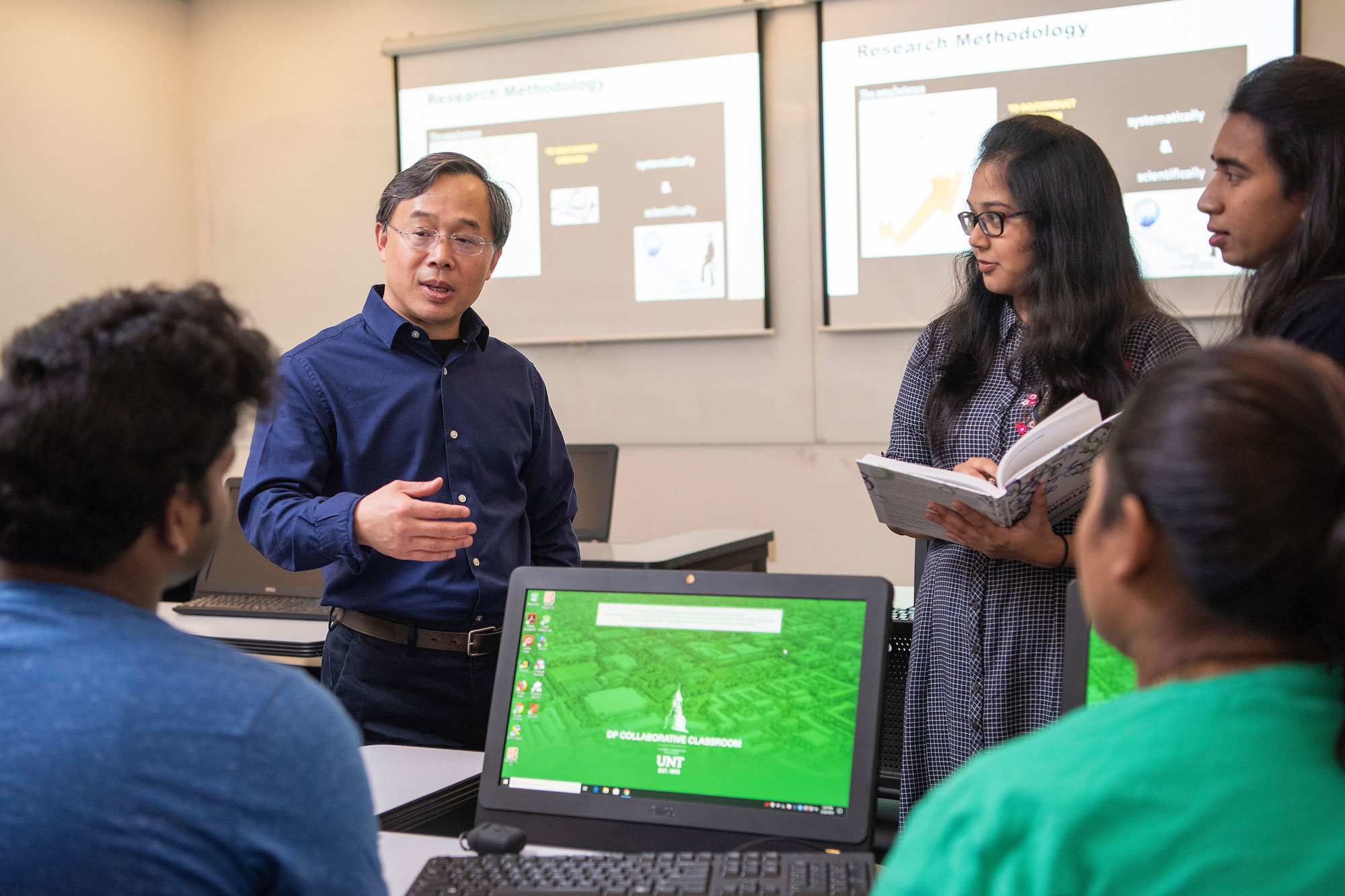 Dr. Junhua Ding speaking to three data science students in classroom.